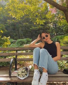 a woman sitting on top of a wooden bench next to a flower pot and sunglasses