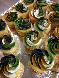 there are many cupcakes with green and black icing on them, sitting on a tray