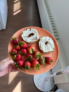 a person holding a plate with strawberries and cream covered donuts on top of it