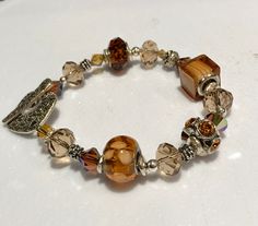 Amber and Topaz tone bracelet featuring a combination of various shaped glass beads and crystals, finished with a gold tone pewter clasp. 8"