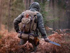 a man with a backpack walking through the woods holding a knife in one hand and wearing a hood on his head