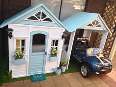 a blue truck parked next to a white house shaped like a toy car with flowers in the windows