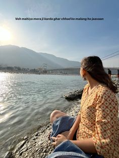 a woman sitting on the shore of a body of water