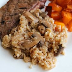 a white plate topped with meat and rice next to carrots, mushrooms and broccoli