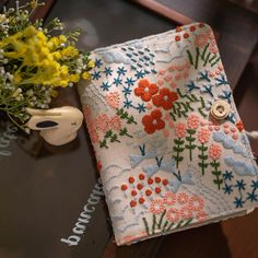 a close up of a cloth on a table with flowers and a vase in the background