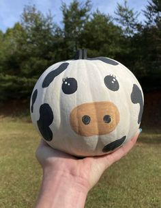 a hand holding up a pumpkin with a cow face painted on it