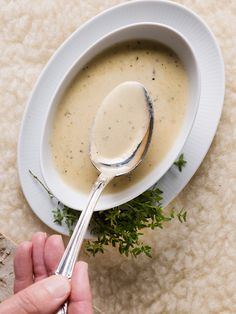 a person is holding a spoon over a bowl of soup with parsley on the side