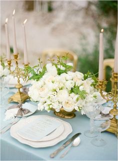 the table is set with white flowers and silverware, candles, and napkins