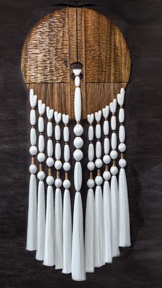 a wooden wall hanging with white beads and tassels