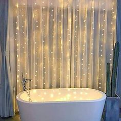 a bathtub with lights on the wall and curtains in front of it, next to a cacti