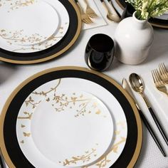 the table is set with black and white plates, silverware, and gold - rimmed utensils