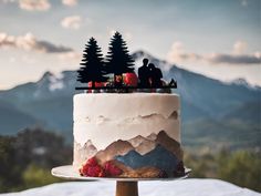 a wedding cake decorated with pine trees and berries on top of a table in front of mountains