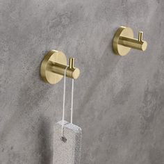 two gold - plated hooks hang on the wall next to a concrete block with a toothbrush holder