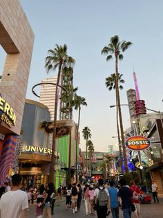 many people are walking down the street in front of shops and buildings with palm trees