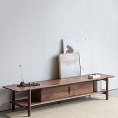 a wooden table sitting on top of a rug next to a white wall with an empty picture frame