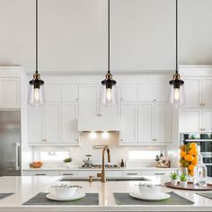 a large kitchen with white cabinets and an island in the middle is lit by three pendant lights