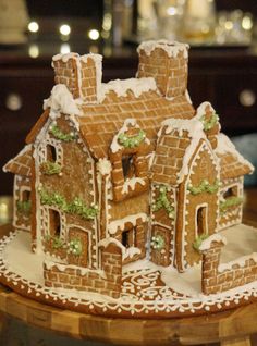 a gingerbread house is decorated with icing and greenery on a wooden table