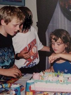 two boys and a girl standing in front of a birthday cake