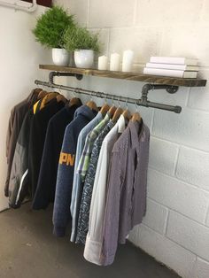 a rack with shirts hanging on it next to a white brick wall and potted plant