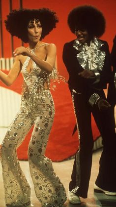 two women in disco outfits standing next to each other with one woman holding her hand out