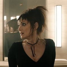 a woman in a black top is staring at something while standing near a mirror with her hair blowing back