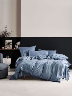 a bed with blue sheets and pillows in a room next to a gray chair on the floor