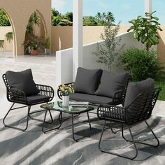 the patio furniture is set up outside on the concrete floor and has gray cushions, black pillows, and a white vase with flowers in it