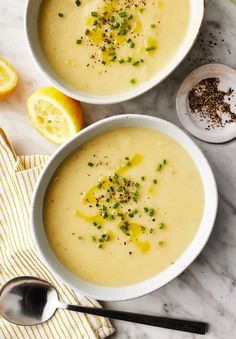 two white bowls filled with soup next to lemons and seasoning on a table