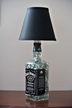 a bottle lamp sitting on top of a wooden table next to a black lampshade