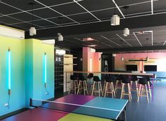 an indoor ping pong table in a brightly colored room with bar stools and neon lights