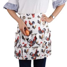 a woman wearing an apron with roosters on it and holding an egg in her hand