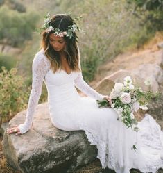 a woman sitting on top of a rock wearing a white dress and holding a bouquet