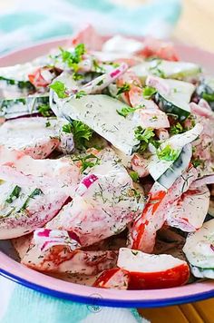 a pink bowl filled with meat and vegetables on top of a tablecloth covered table