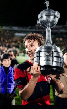 a man holding up a trophy in front of his face with other people behind him