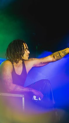 a man with dreadlocks sitting on a chair in front of blue and green lights