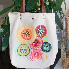 a white bag with colorful images on it hanging from a planter next to a potted plant