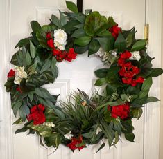 a wreath with red and white flowers hanging on a door