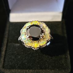 This Elite Shungite And Ethiopian Welo Opal Ring Is Designed With A Flower In Mind The Elite Shungite Ring Has An Adorable Floral Look That Is Beautiful, Elegant, And Will Definitely Have Heads Turned Your Way This Ring Features A Single Round Elite Shungite Gemstone That Is Surrounded By Beautiful Ethiopian Welo Opal Gemstones This Ring Is Crafted In Platinum Over Sterling Silver Shungite Gemstone Is Approx 2.50ctw And Is Appox 10mm In Size There Are 10 Welo Ethiopian Opals That Are Approx 1.25 Black Multi-stone Round Rings, Black Gemstone Rings For Healing, Black Opal Gemstone Ring, Elegant Black Opal Ring Gift, Elegant Black Opal Ring As Gift, Elegant Black Opal Ring For Gift, Black Flower Ring For Wedding, Elite Shungite, Beautiful Ethiopian