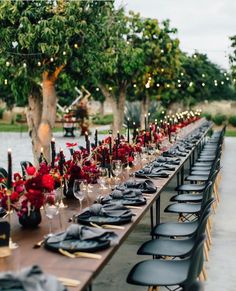 a long table is set with black plates and red flowers