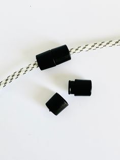 three black plastic plugs on a white cord with two wires connected to them and one has an end cap in the middle