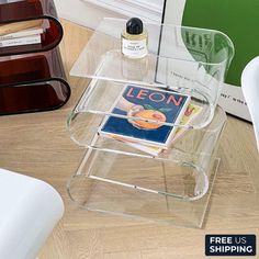 a glass table with a magazine on it next to a white chair and a book