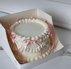 a white cake in a box with pink ribbon around it's edges and on the inside