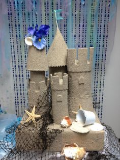 a castle made out of sand with shells and seashells on the table next to it