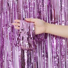 a hand is reaching for some purple tinsel wrapped in plastic streamers on the wall