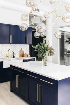 a kitchen with blue cabinets, white counter tops and an island in the center is decorated with hanging glass globes