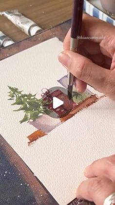 a person is using a pen to paint an image on paper with watercolors