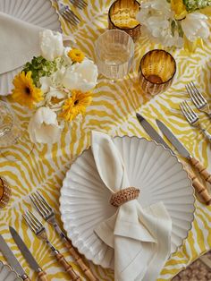 a yellow and white table setting with napkins, silverware and flowers on it