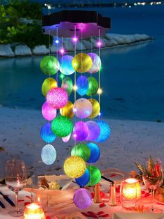 a table topped with lots of different colored balls hanging from it's ceiling next to water