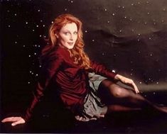 a woman sitting on the ground with her legs crossed and looking at the camera, in front of stars