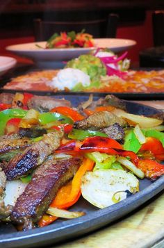 a plate full of meat and vegetables on a table with other plates in the background